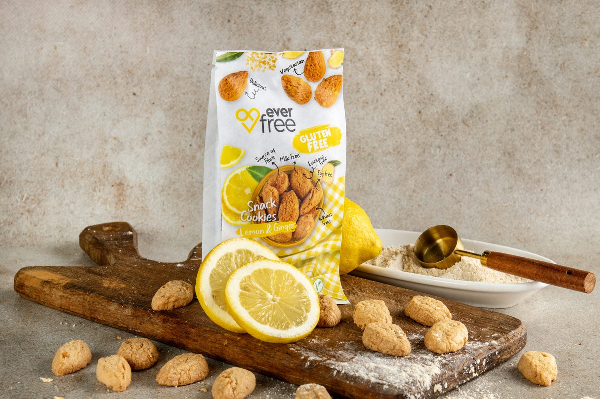 EverFree Lemon & Ginger Gluten-Free Cookies bag on a wooden board with fresh lemon, loose cookies and a bowl of flour